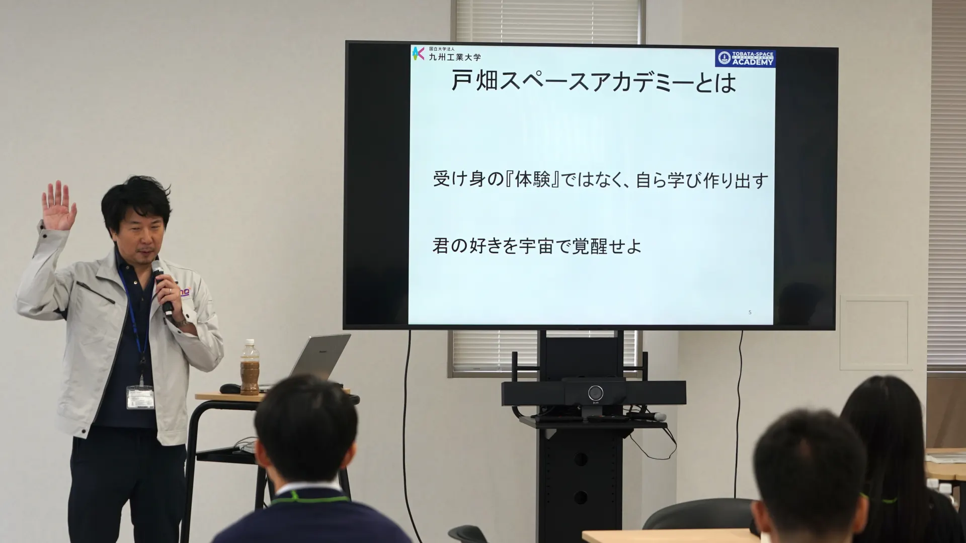 「戸畑スペースアカデミーとは：受け身の『体験』ではなく、自ら学び作り出す／君の好きを宇宙で覚醒せよ」のスライドを背に語る布施哲人アカデミー長