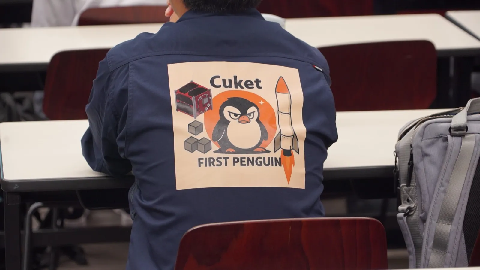 衛星プロジェクト「Cuket」のペンギンのワッペンが付いた学生の作業着の背中